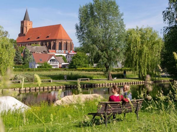 2 Frauen sitzen auf einer Bank und blicken über die Spree auf die St. Mrienkirche in Beeskow