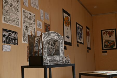Raum mit Bilder an den Wänden und davor Tisch mit Ausstellungsstück
