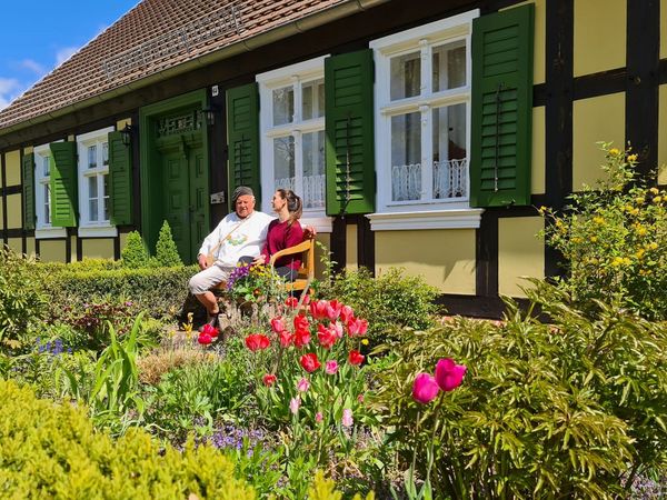 Zwei Menschen sitzen auf einer Bank vor einem Haus in historischen Kolonistendorf Neulietzegöricke im Oderbruch.