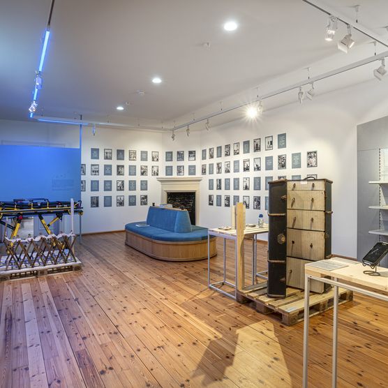 großer Ausstellungsraum mit Bilder an den Wänden, großer Kofer in der Mitte und Trage