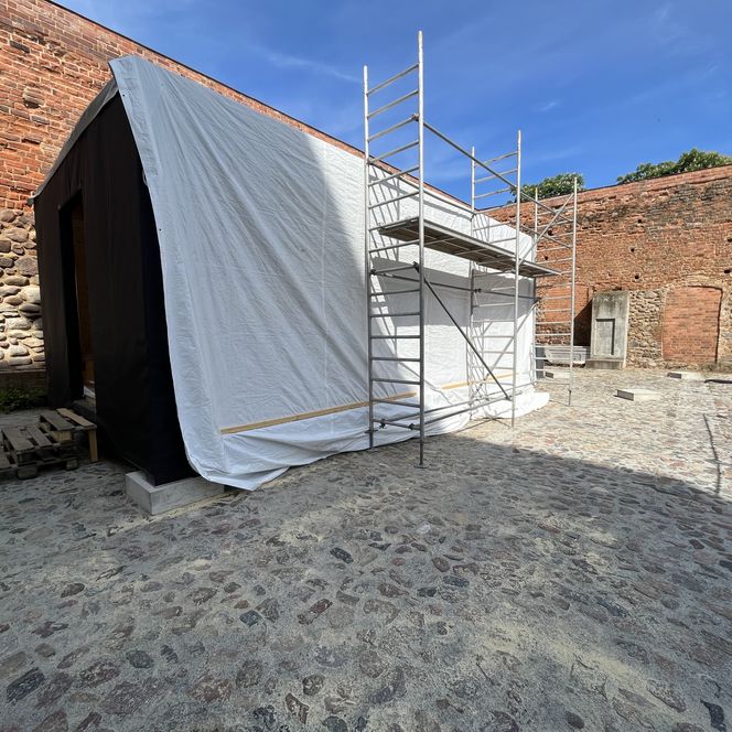 alte Mauer und davor ein Teil der Burghofbühne mit Gerüst und verhüllt